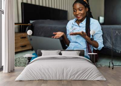 Confused young African American woman at home sitting in casual jeans on the floor in the living room using a laptop Wall mural